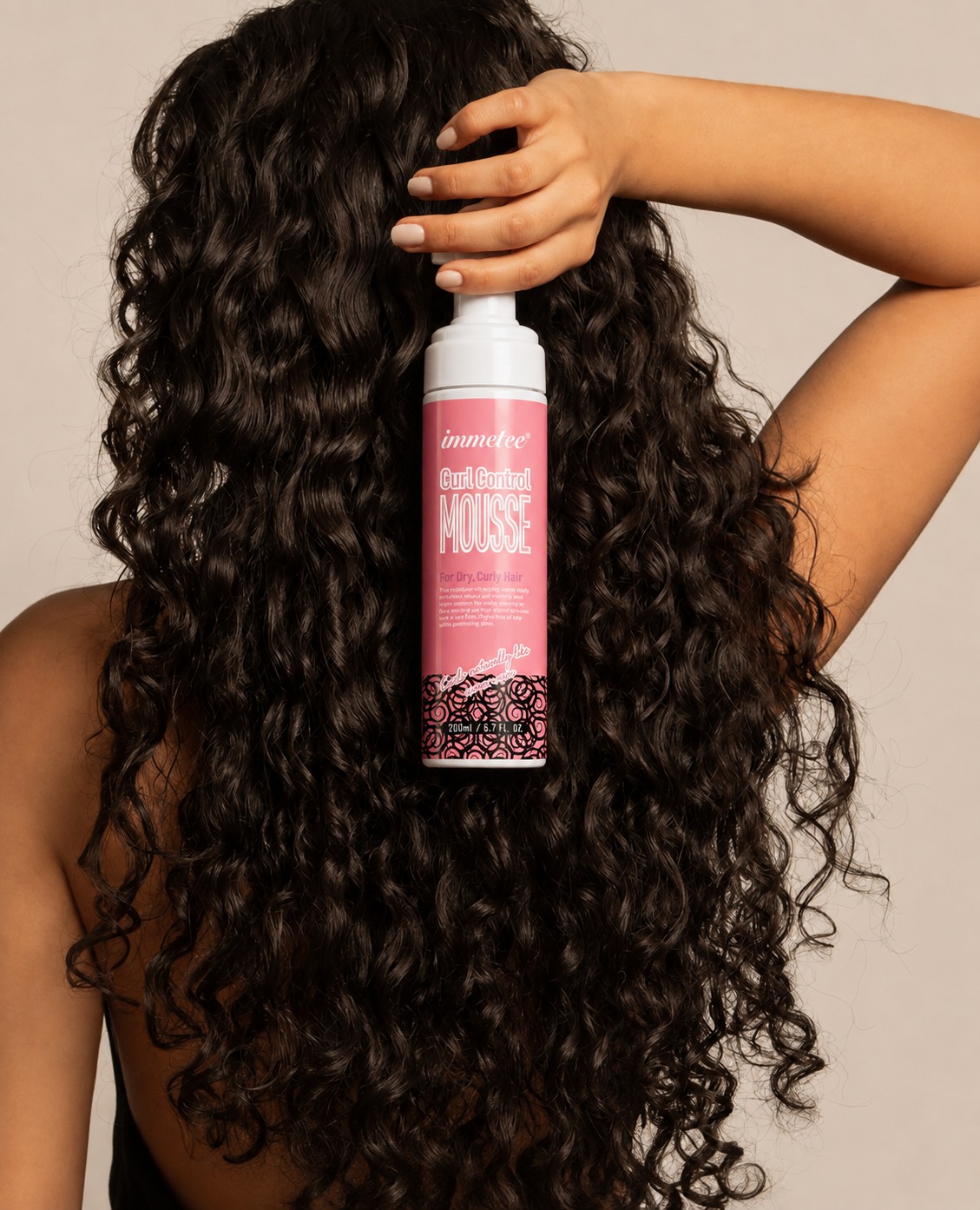 Woman with long defined curls holding immetee Curl Control Mousse